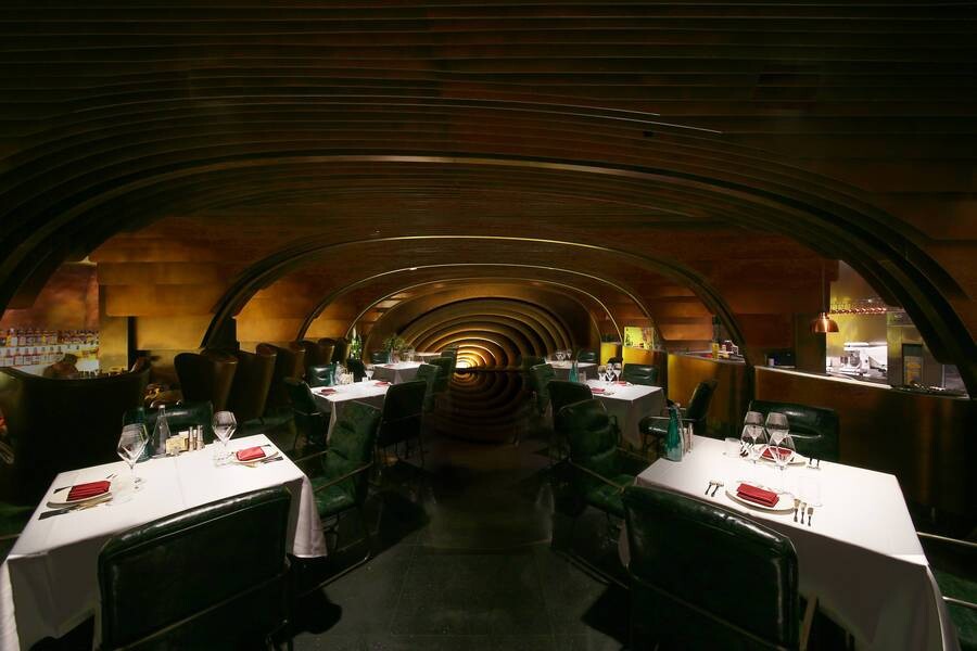First-floor public dining space of the MS-II Restaurant, where curved bronze plates and arch elements organize seating and circulation.