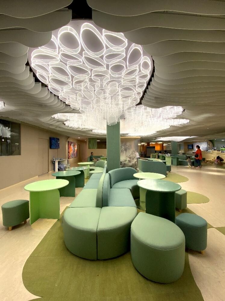 Second-floor public area of the children’s learning center, with green furniture and tree-like lighting expressing a nature-inspired open learning space.