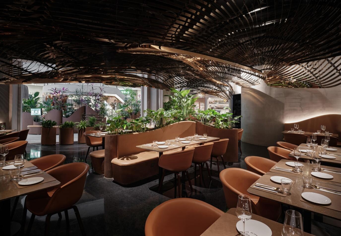 Dining area covered by layered metal roof installations, with tables, planting, and curved seating forming flexible island-like dining zones.