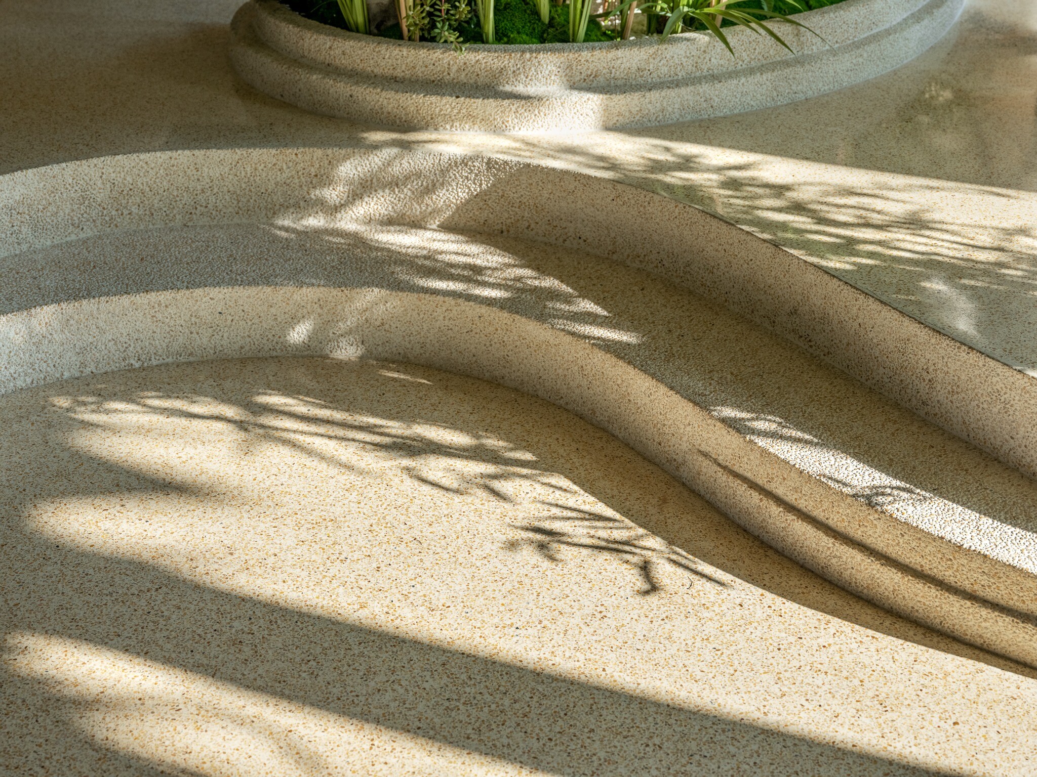 Natural light passing through bamboo leaves and casting shadows on wall and stone surfaces, creating layered bamboo-shadow effects.